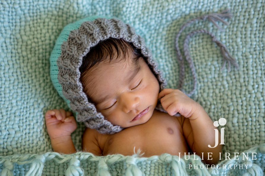 newborn baby boy in teal bed with bonnet