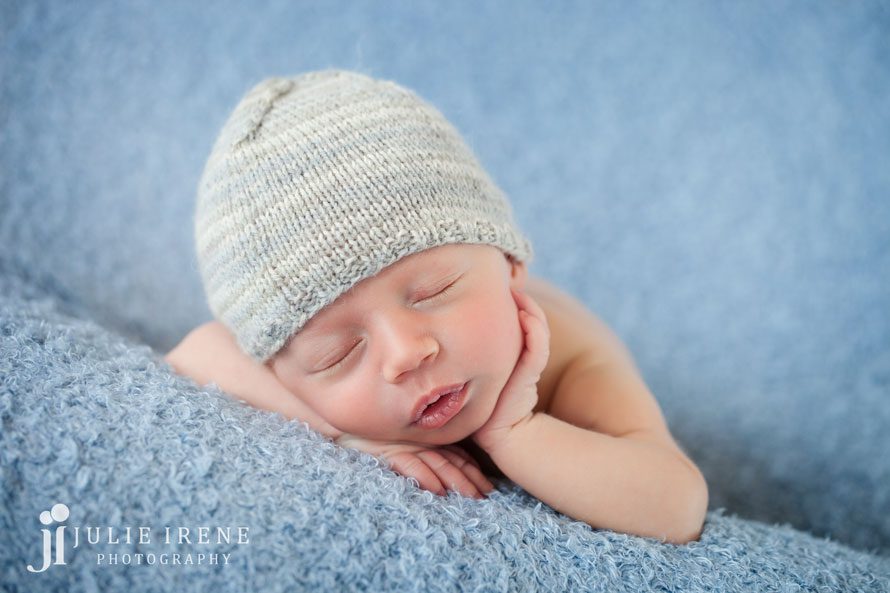 hand on cheek with knit hat and blue blanket newborn photo