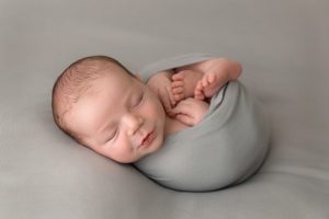 adorable newborn boy wrapped in a simple gray wrap