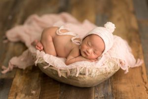 newborn girl on barn wood floor in light pinks