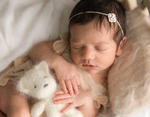 close up of newborn girl holding knitted teddy bear