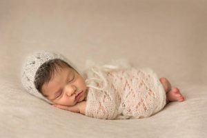 newborn wrapped in a pretty knit laying on cream blanket