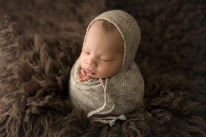 boy wrapped in knitted hat and wrap on dark brown flokati