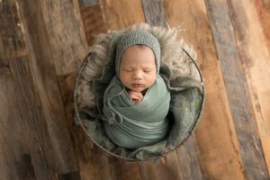 green sage newborn boy wrapped and in a prop