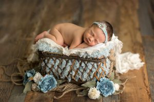 newborn girl with blue flowers in a weaved basket