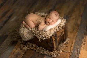 newborn boy in vintage wooden crate with neutrals and a cream pillow
