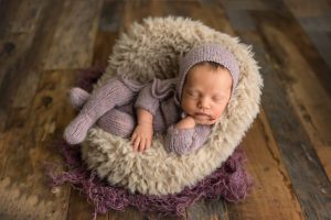 newborn girl in knitted purple outfit sitting in a chair