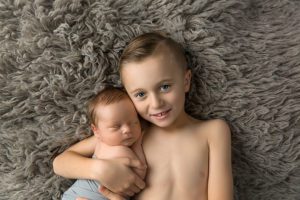 newborn boy with child sibling brother on gray flokati