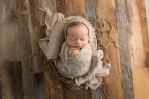 neutral baby boy wrapped in prop with knitted outfit