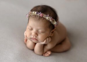 newborn girl with floral headband in froggy pose side angle
