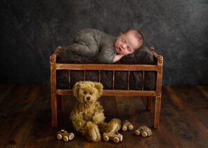 newborn boy laying in a bed with a teddy and toys