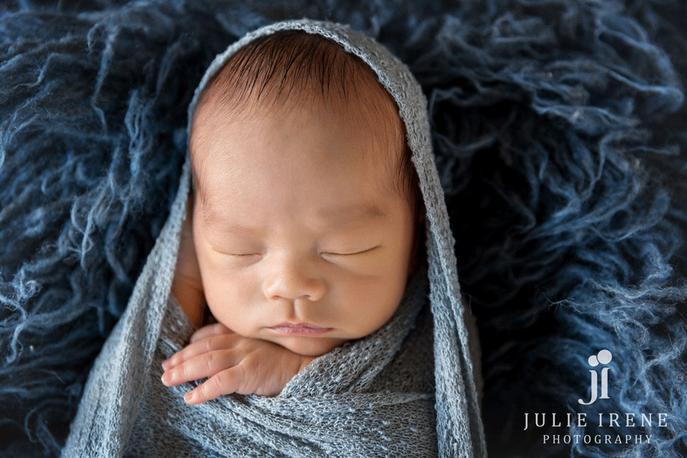 Newborn wrapped in steel blue on a navy rug