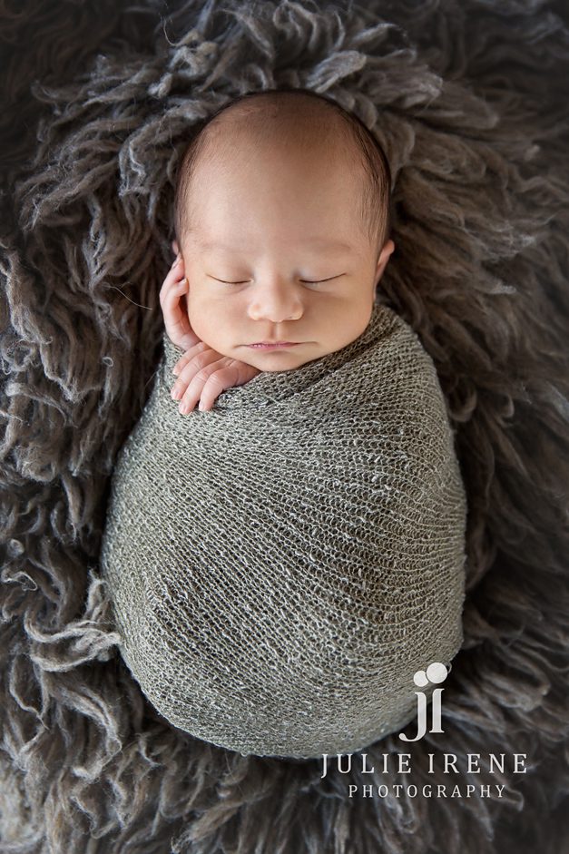 newborn baby boy wrapped in gray hand on cheek