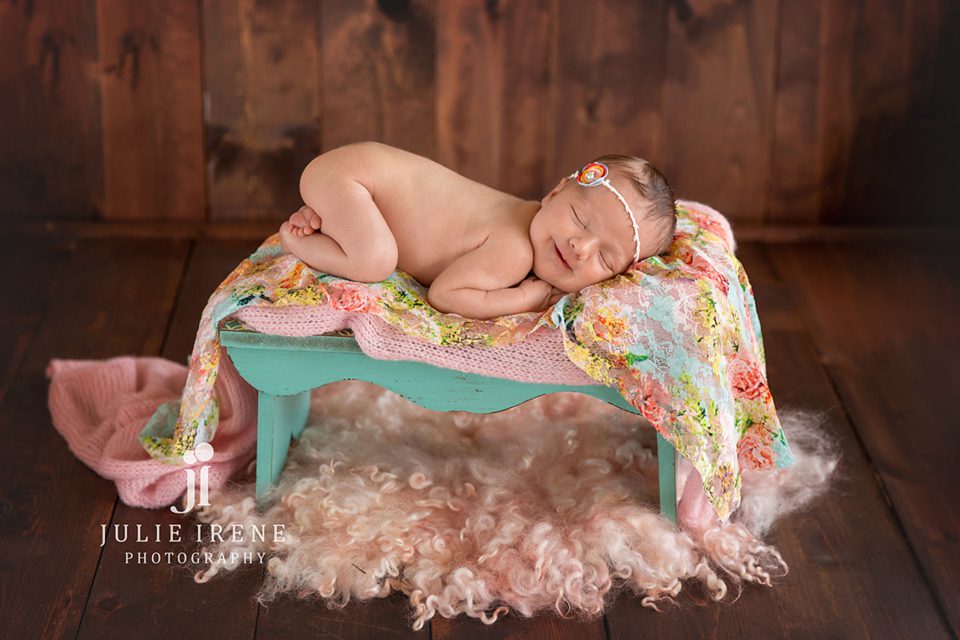 newborn girl with teal and pink floral wrap and smiles