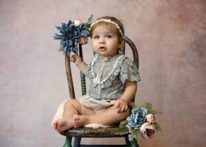 cute 12 month old girl sitting in vintage chair with flowers