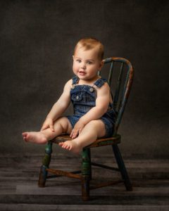 one year old boy with overalls sitting in a vintage chair