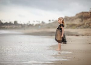 little girl staring at ocean in a dress
