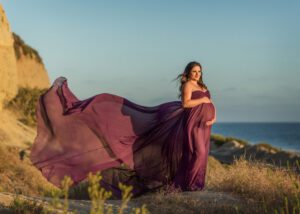 Pregnant woman in flowing purple gown on the cliffs at San Clemente beach at golden hour